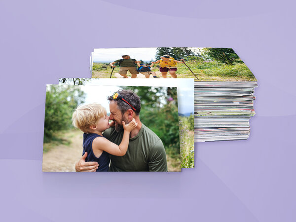 Großer Stapel Fotoabzüge mit Natur- und Familienmotiven, vorne ein Vater mit Kind in innigem Moment.