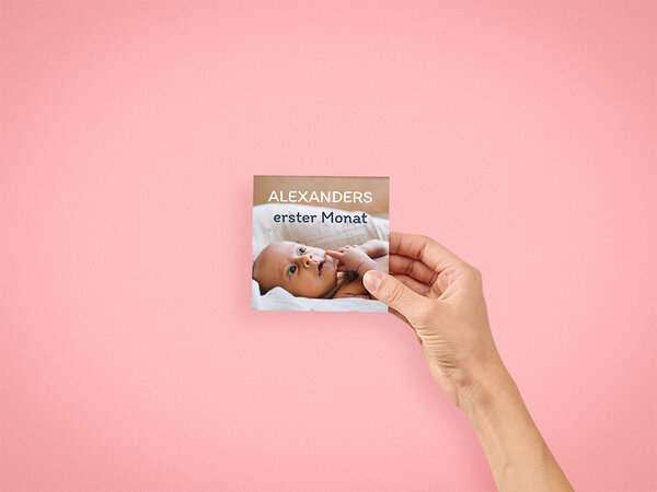 Auf dem Cover eines 10x10 cm Fotobuchs ist ein Bild eines Babys. Das Fotobuch wird dabei mit der rechten Hand gehalten. 