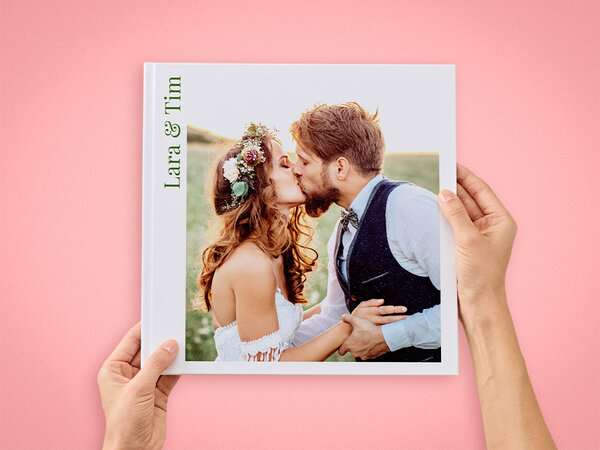 Ein Fotobuch im Format 30x30 wird von zwei Händen gehalten. Auf dem Cover ist ein Bild eines verliebtes Hochzeitspaars. 